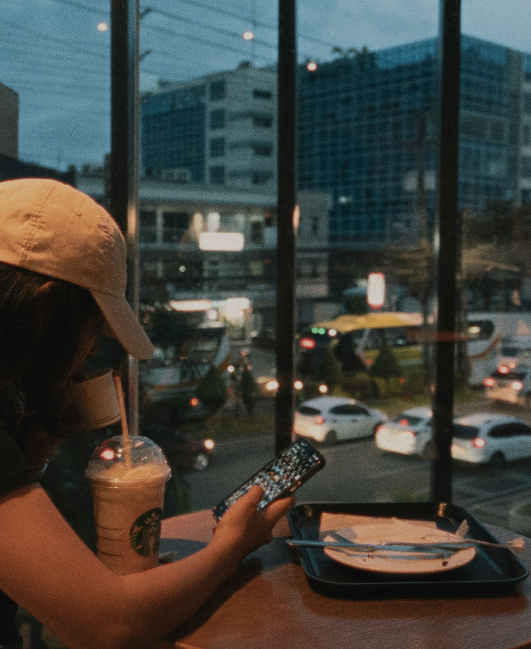 Frau im Café am Abend, Blick aufs Handy vor der Stadt